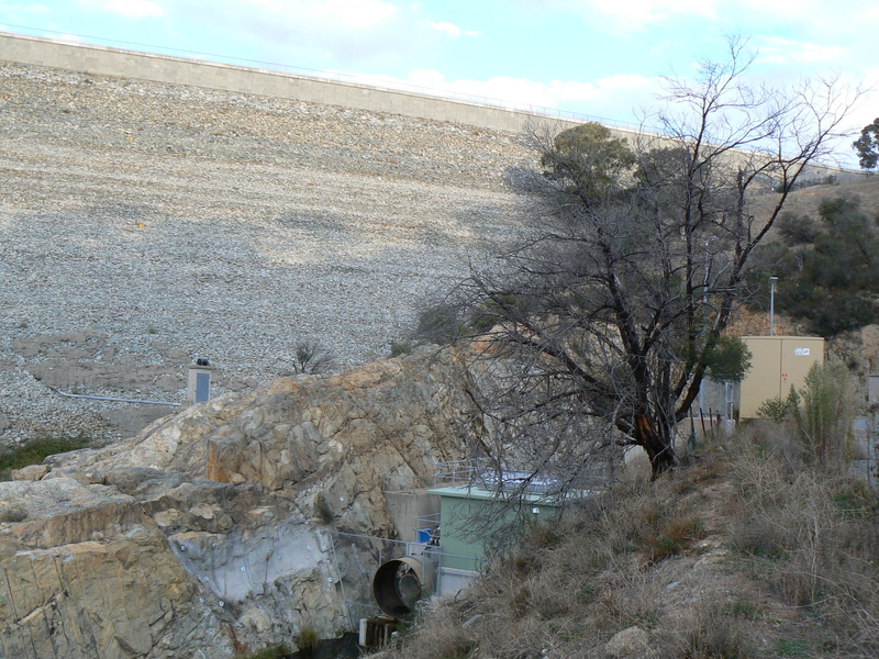 The right side of the dam wall as seen from the base of the "dry" side, plus what appears to be a door in the wall, and the pumping system feeding the environmental flow in to the Queanbeyan River. There is a powerline running from the substation near the pumping station to this pump.